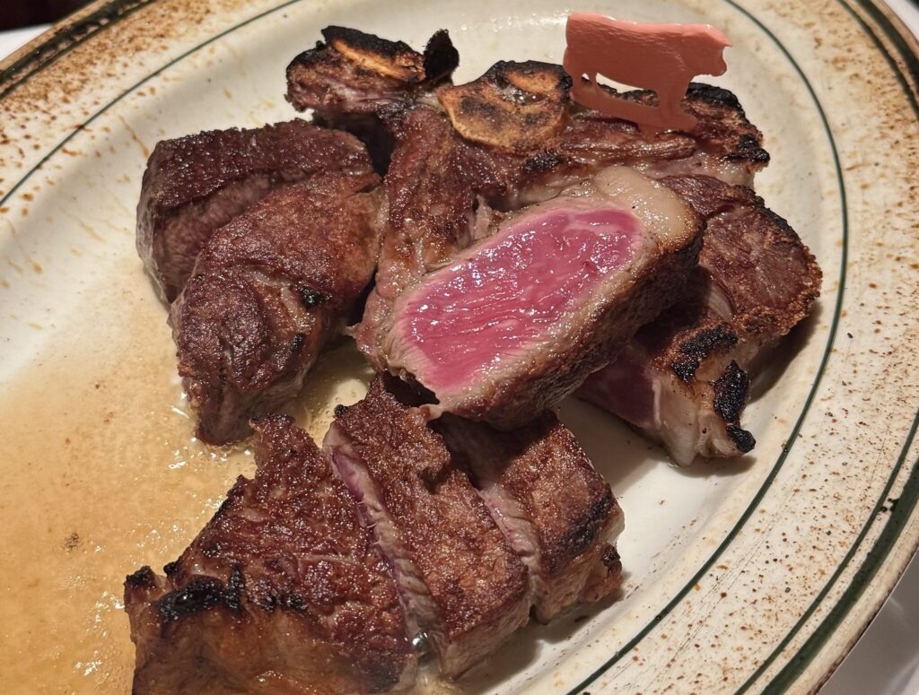 断面がピンク色のTボーンステーキ。骨付きで切り分けられ、牛のピックがのっている