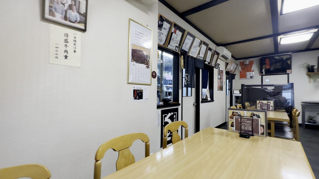 木のテーブルが並ぶ店内。壁にサイン色紙が飾られている