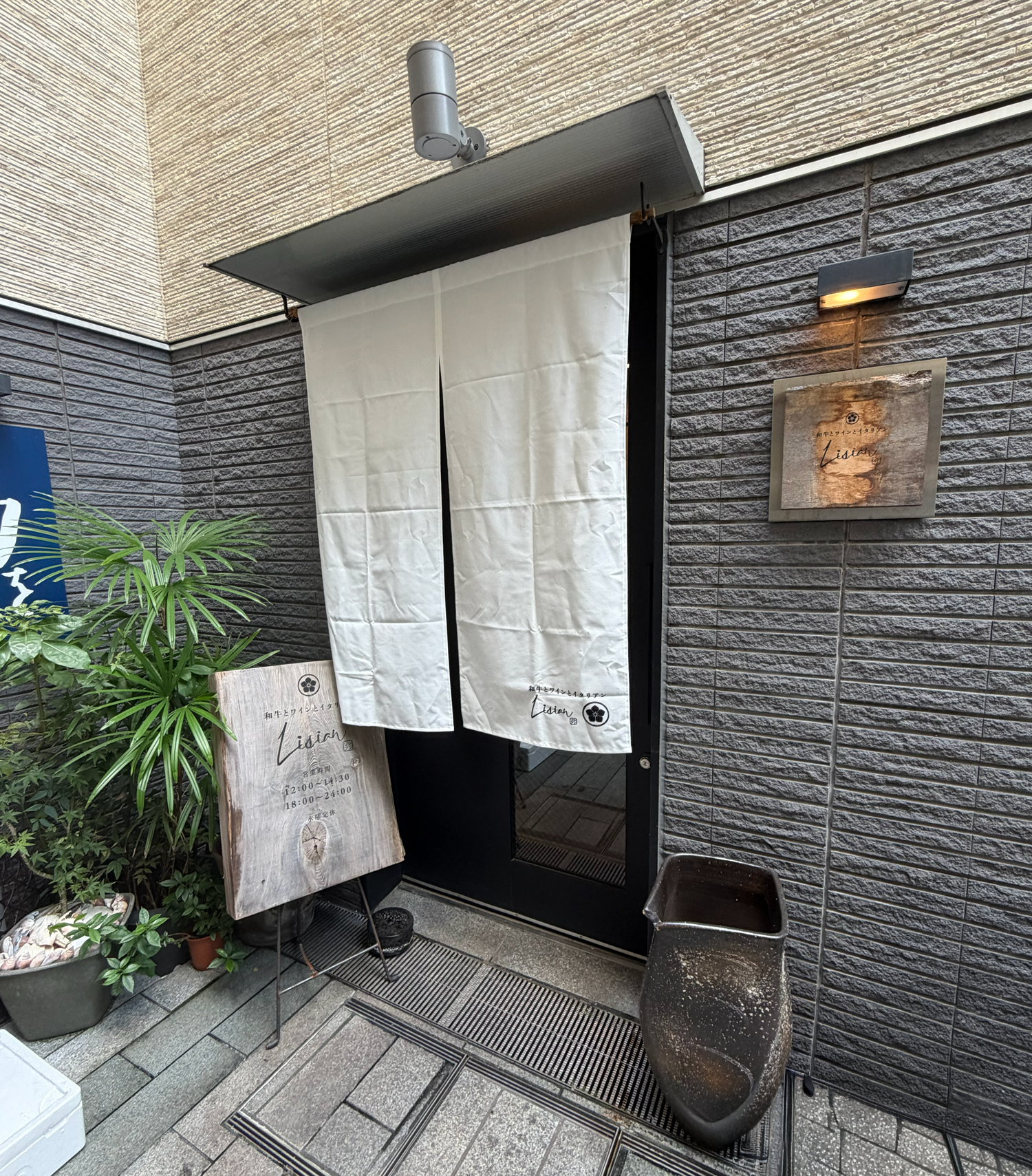 白い暖簾と木製の看板があるLisianの入口