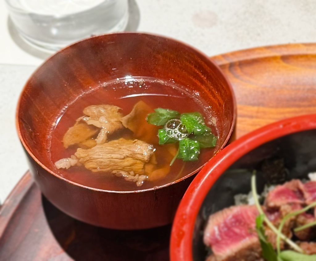 赤いお椀に入った肉吸い。お肉と三つ葉が見える